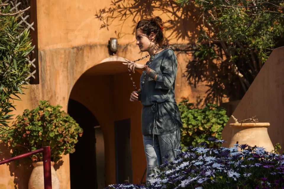 Femme en tunique grise et pantalon clair parmi les jardins de Porquerolles.