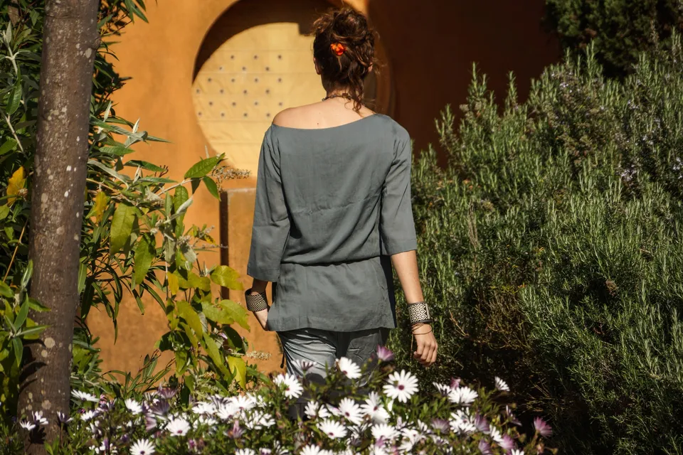 Femme en tunique grise et pantalon clair parmi les jardins de Porquerolles.