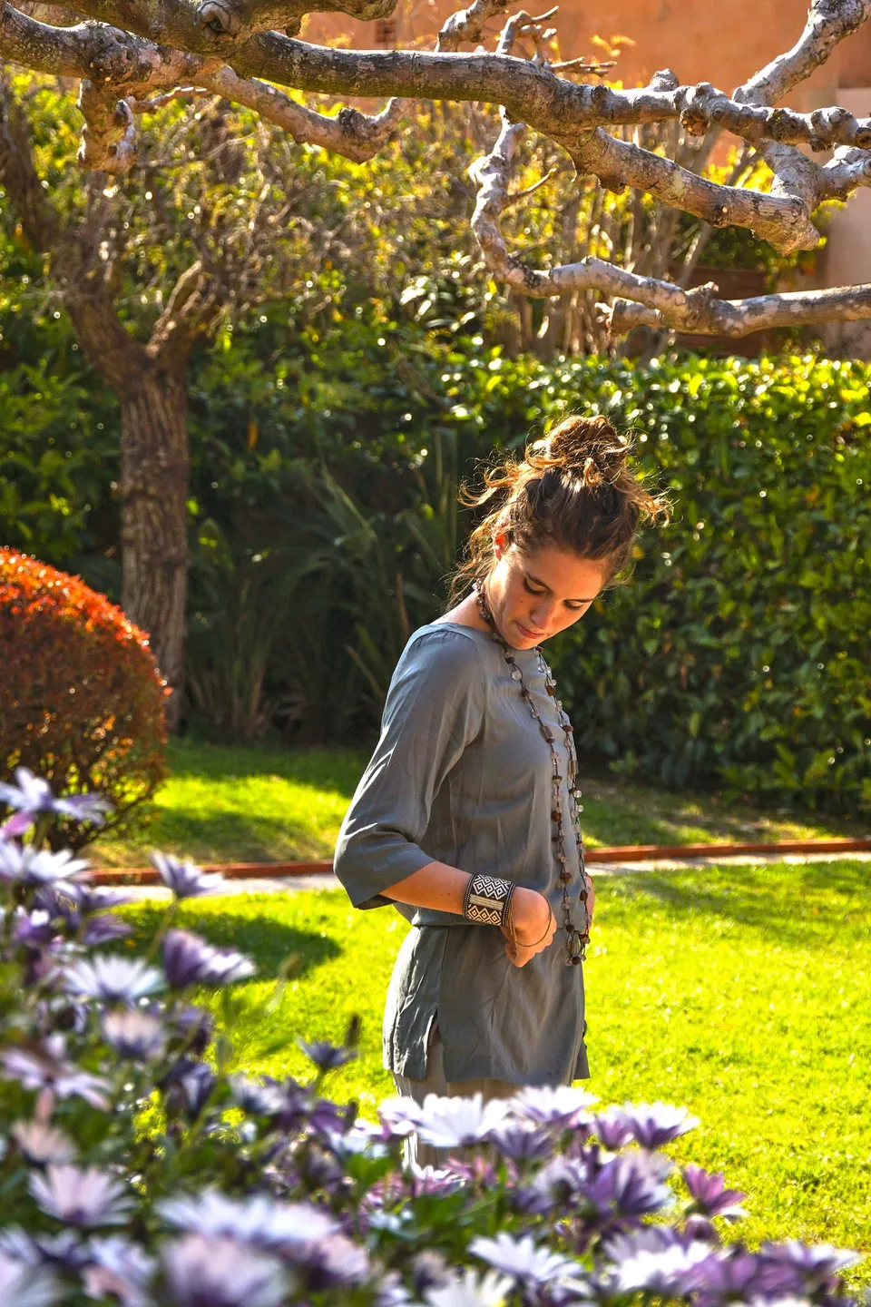 Femme en tunique grise et pantalon clair parmi les jardins de Porquerolles.