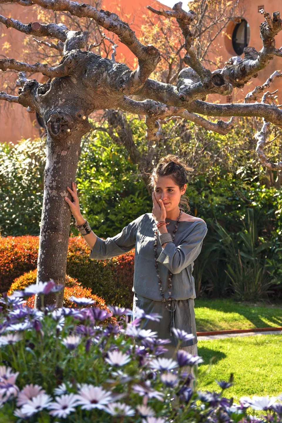 Femme en tunique grise et pantalon clair parmi les jardins de Porquerolles.