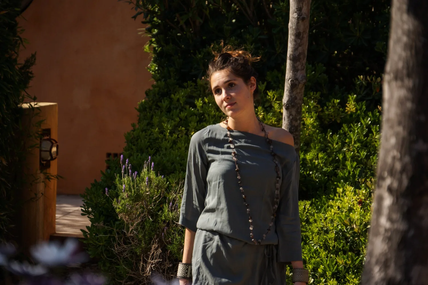 Femme en tunique grise et pantalon clair parmi les jardins de Porquerolles.
