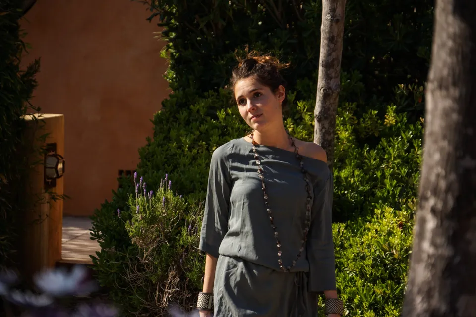 Femme en tunique grise et pantalon clair parmi les jardins de Porquerolles.