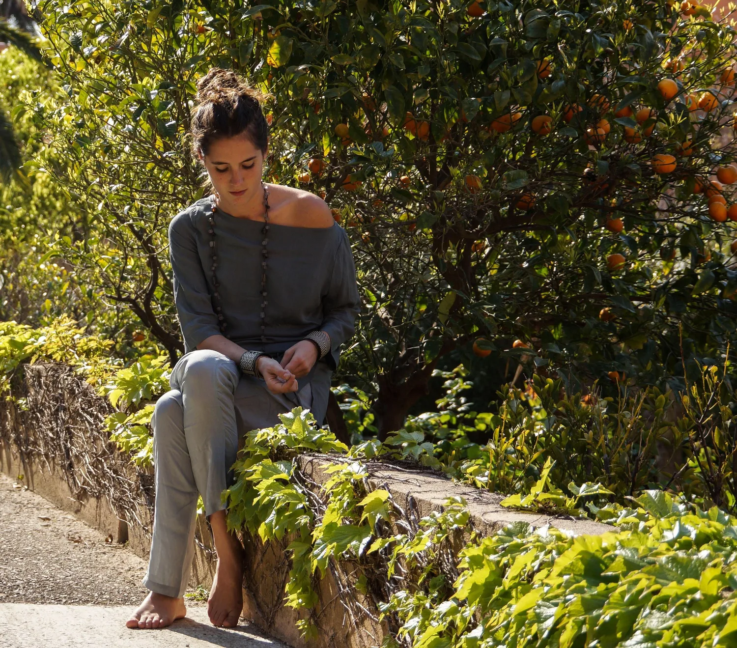 Femme en tunique grise et pantalon clair parmi les jardins de Porquerolles.