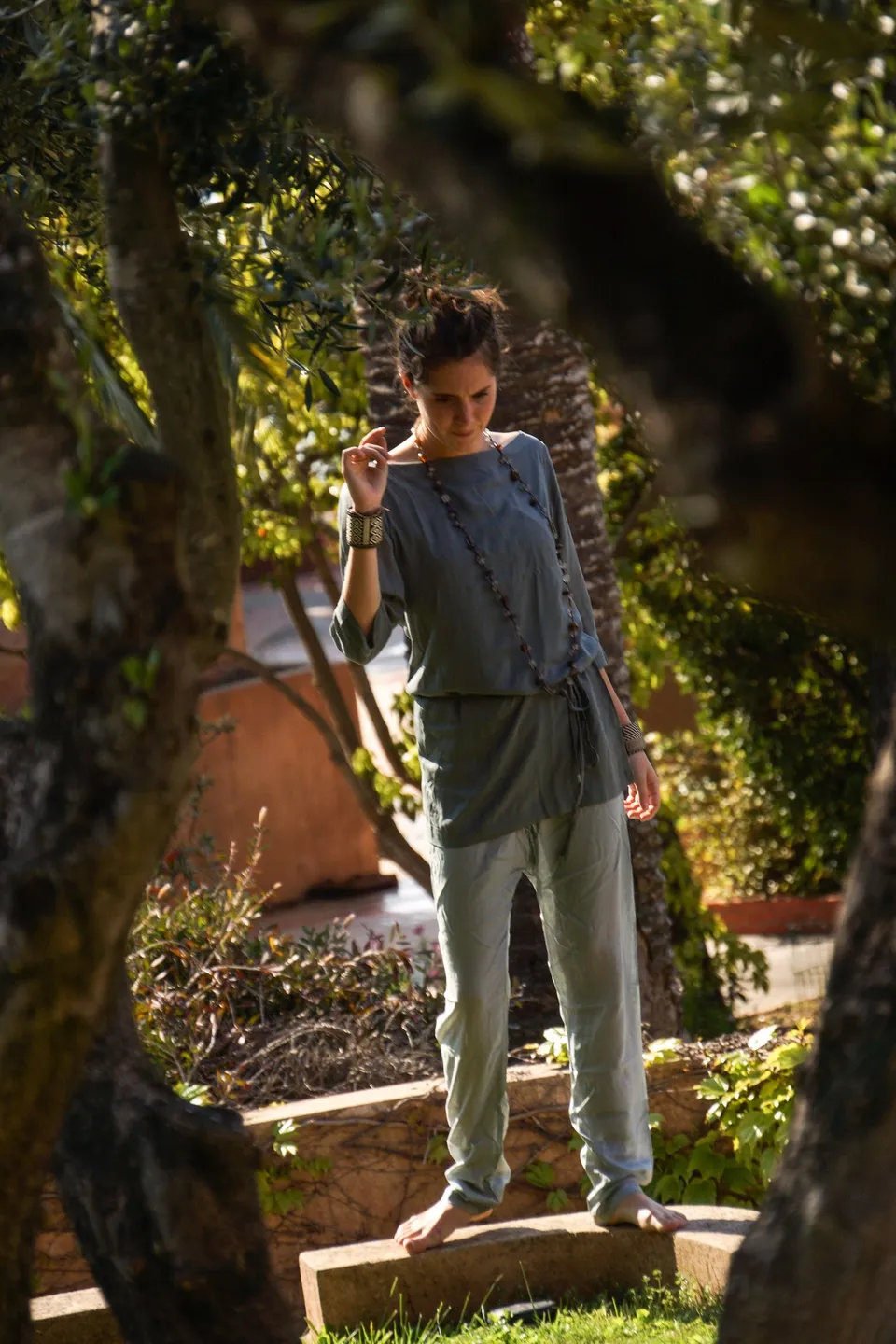 Femme en tunique grise et pantalon clair parmi les jardins de Porquerolles.