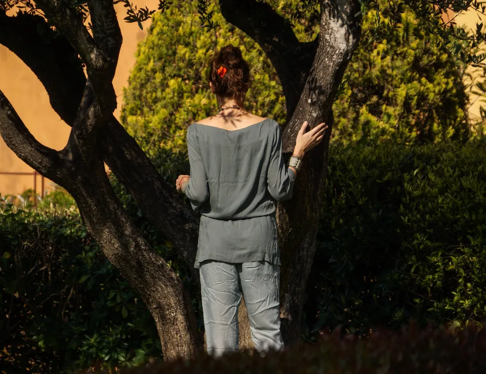 Femme en tunique grise et pantalon clair parmi les jardins de Porquerolles.