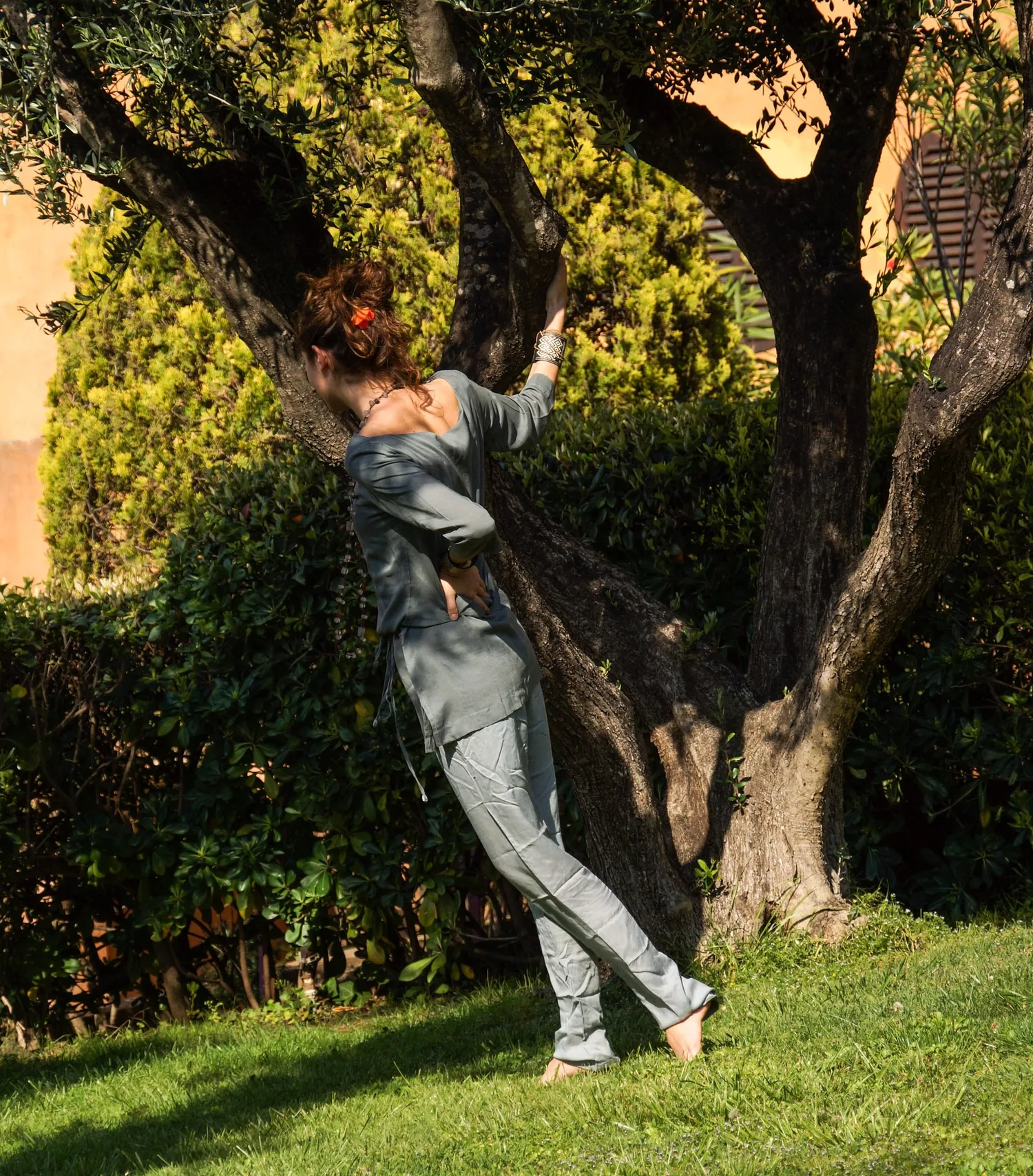 Femme en tunique grise et pantalon clair parmi les jardins de Porquerolles.