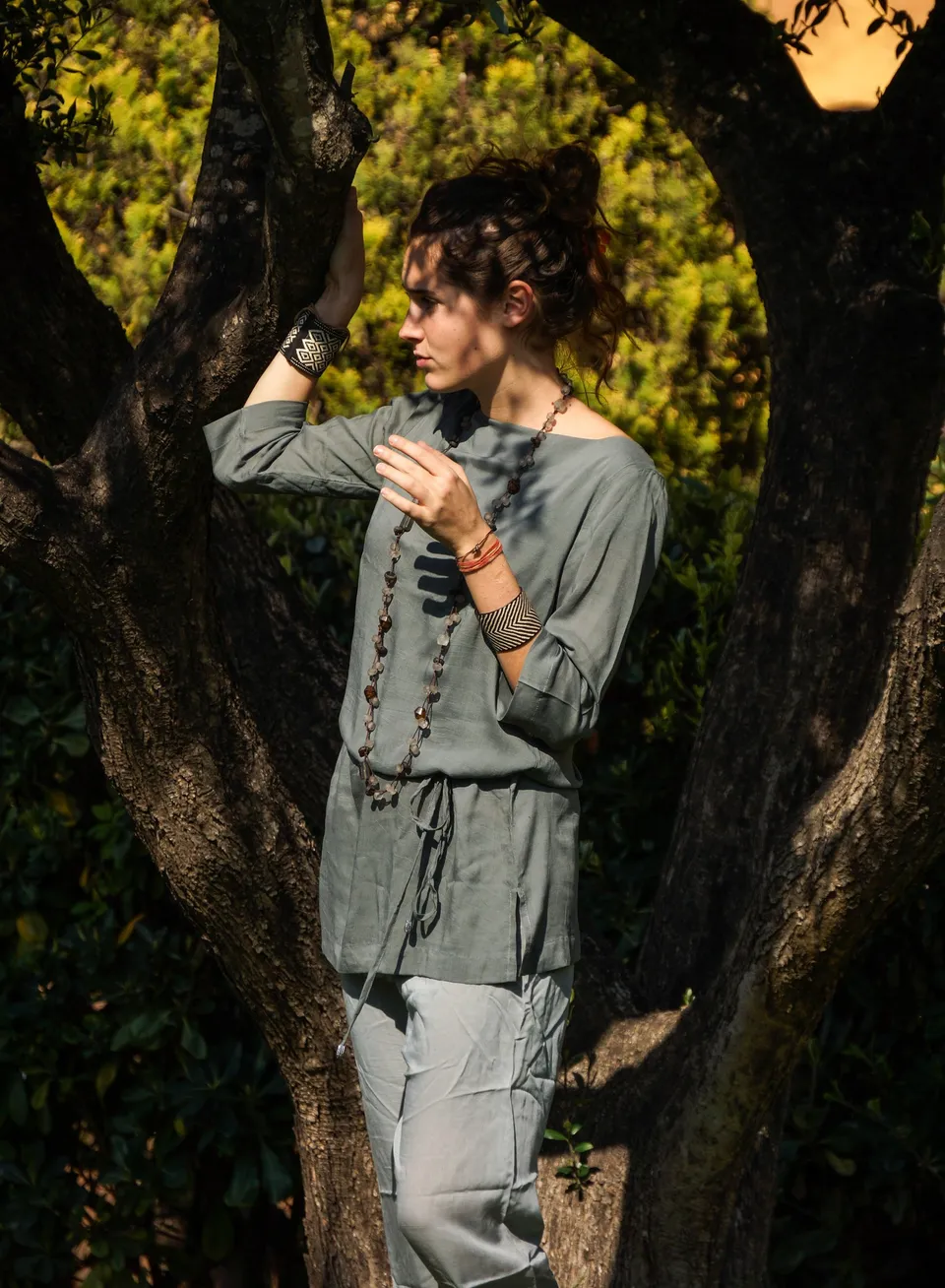 Femme en tunique grise et pantalon clair parmi les jardins de Porquerolles.