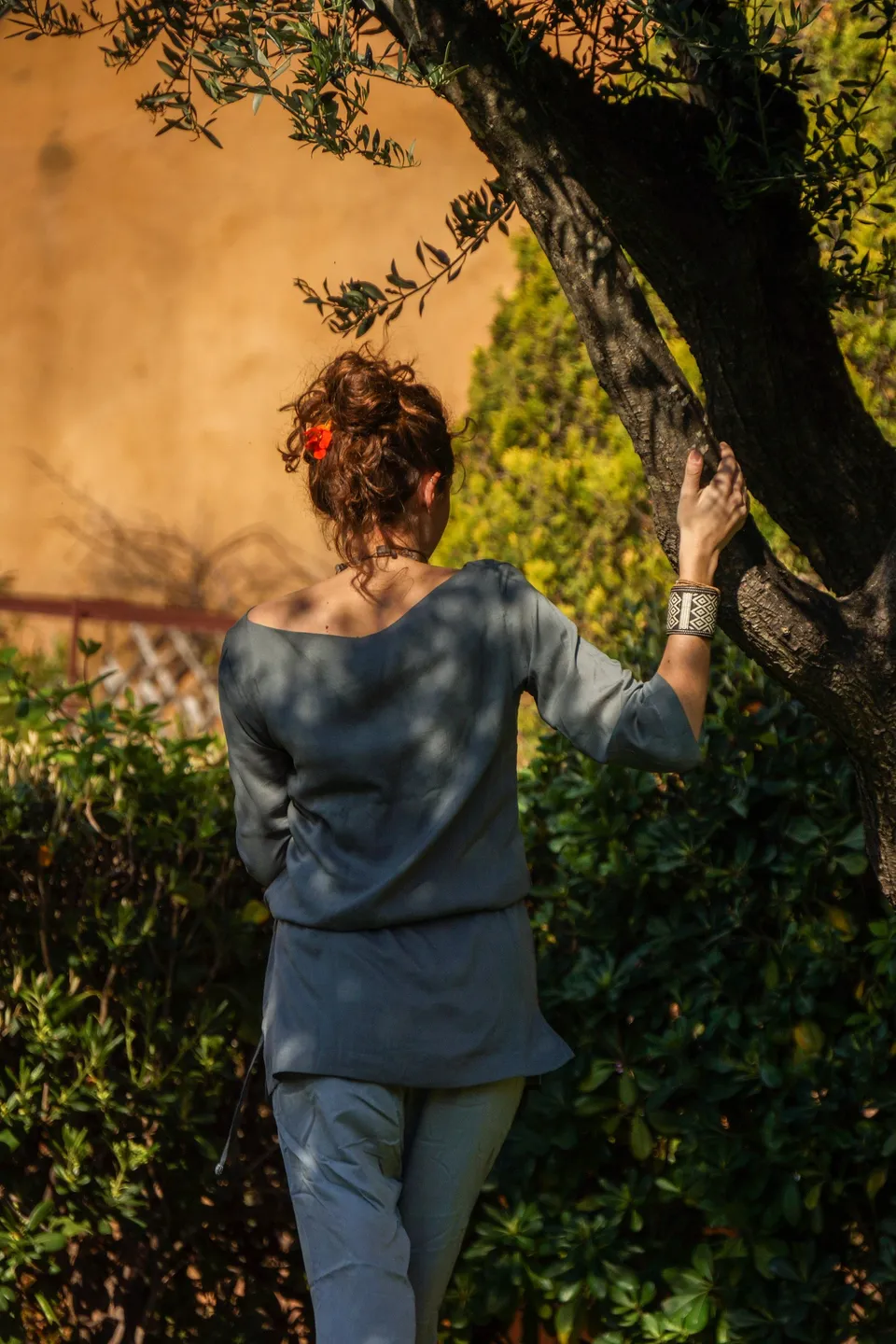 Femme en tunique grise et pantalon clair parmi les jardins de Porquerolles.