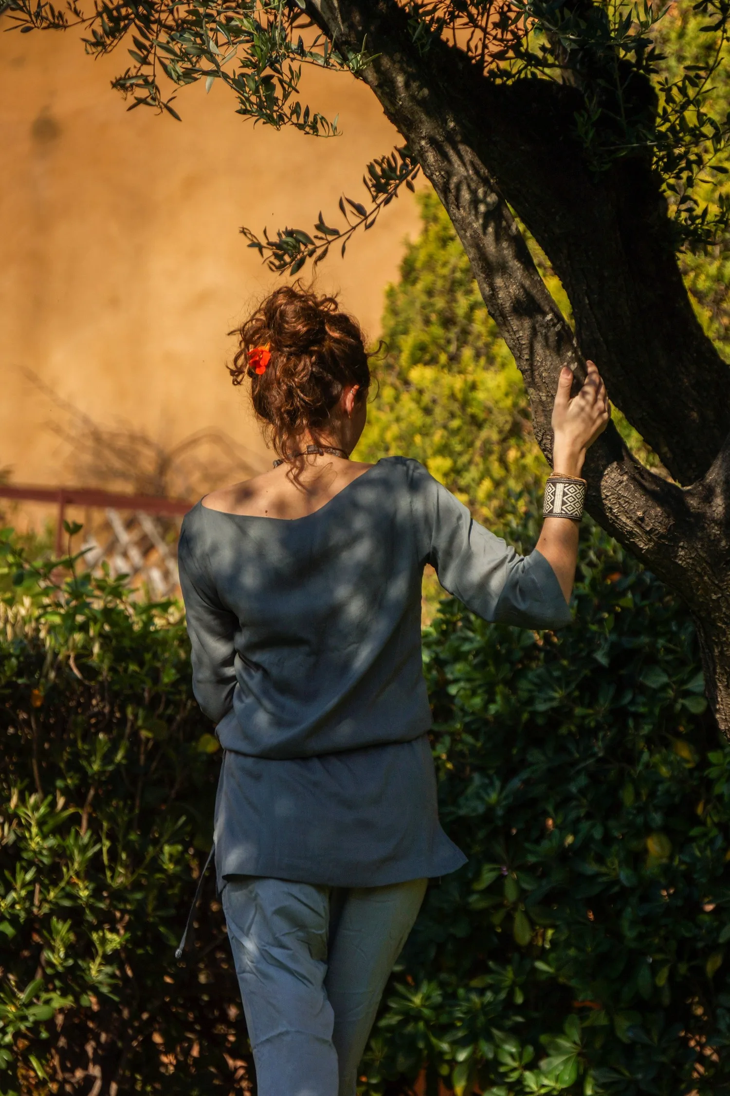 Femme en tunique grise et pantalon clair parmi les jardins de Porquerolles.