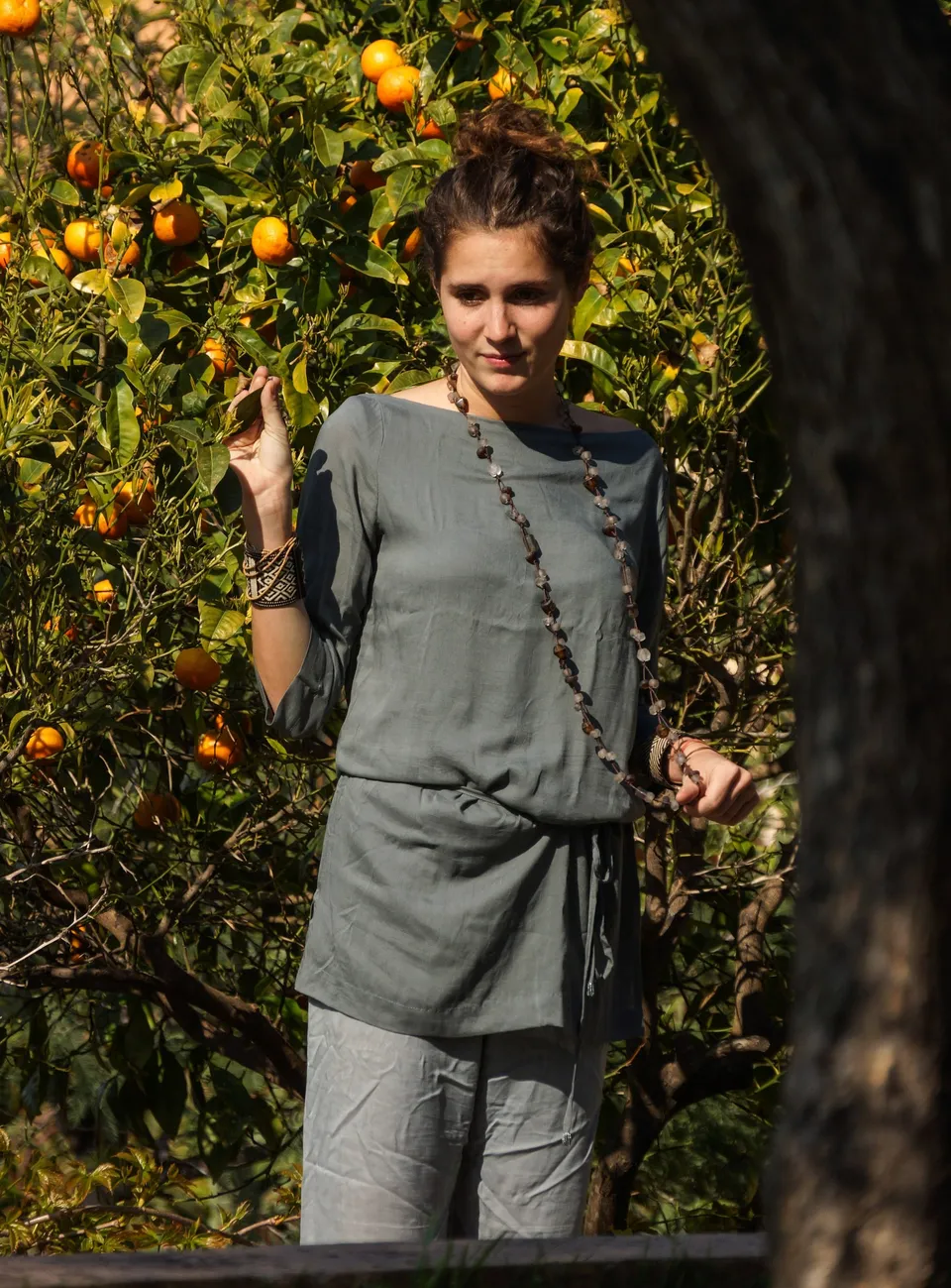 Femme en tunique grise et pantalon clair parmi les jardins de Porquerolles.
