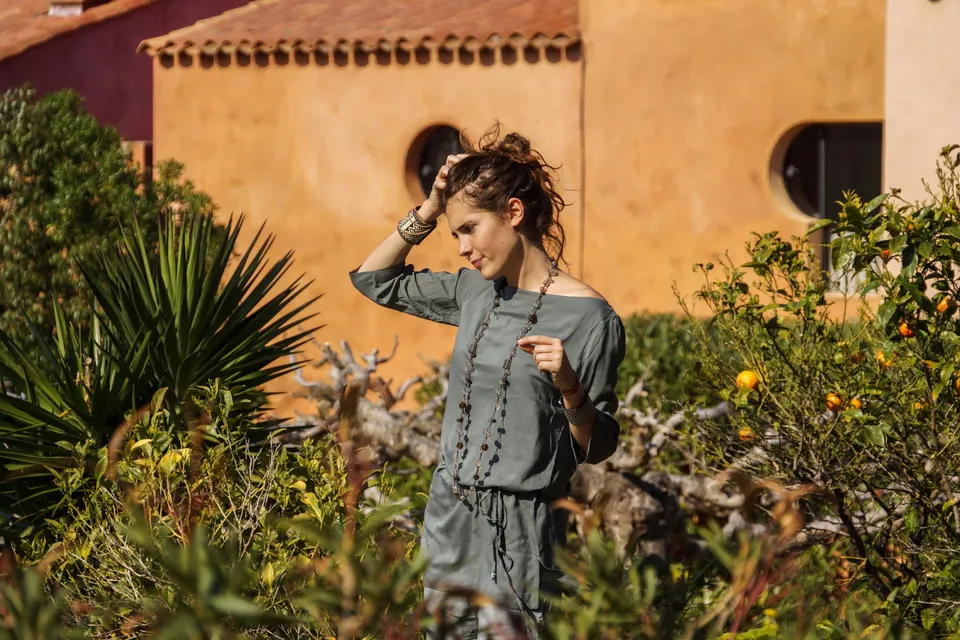 Femme en tunique grise et pantalon clair parmi les jardins de Porquerolles.