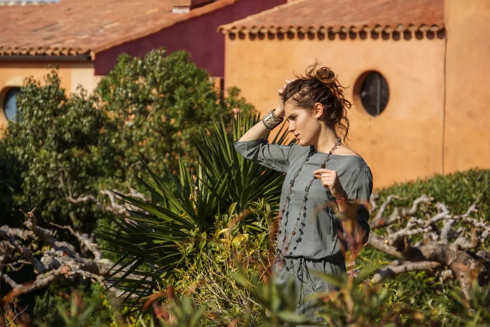 Femme en tunique grise et pantalon clair parmi les jardins de Porquerolles.