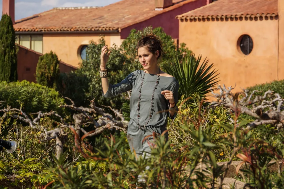 Femme en tunique grise et pantalon clair parmi les jardins de Porquerolles.