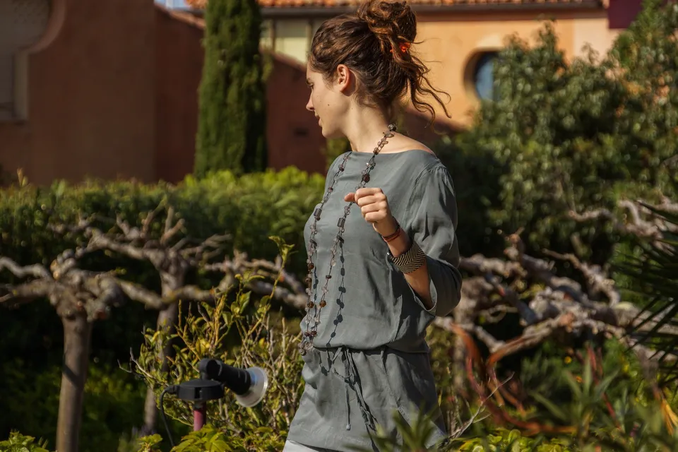 Femme en tunique grise et pantalon clair parmi les jardins de Porquerolles.