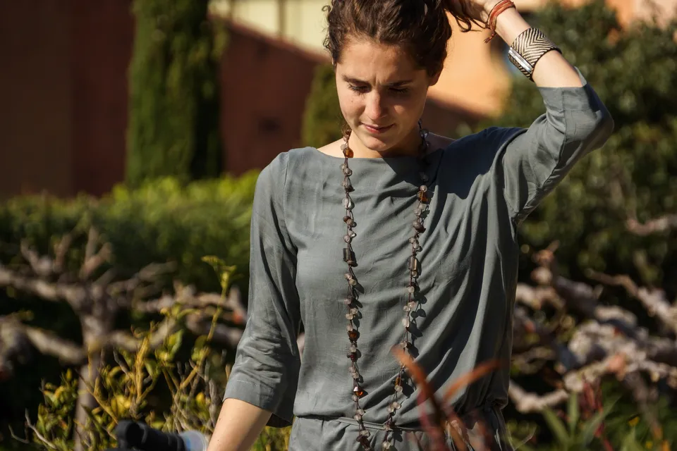 Femme en tunique grise et pantalon clair parmi les jardins de Porquerolles.