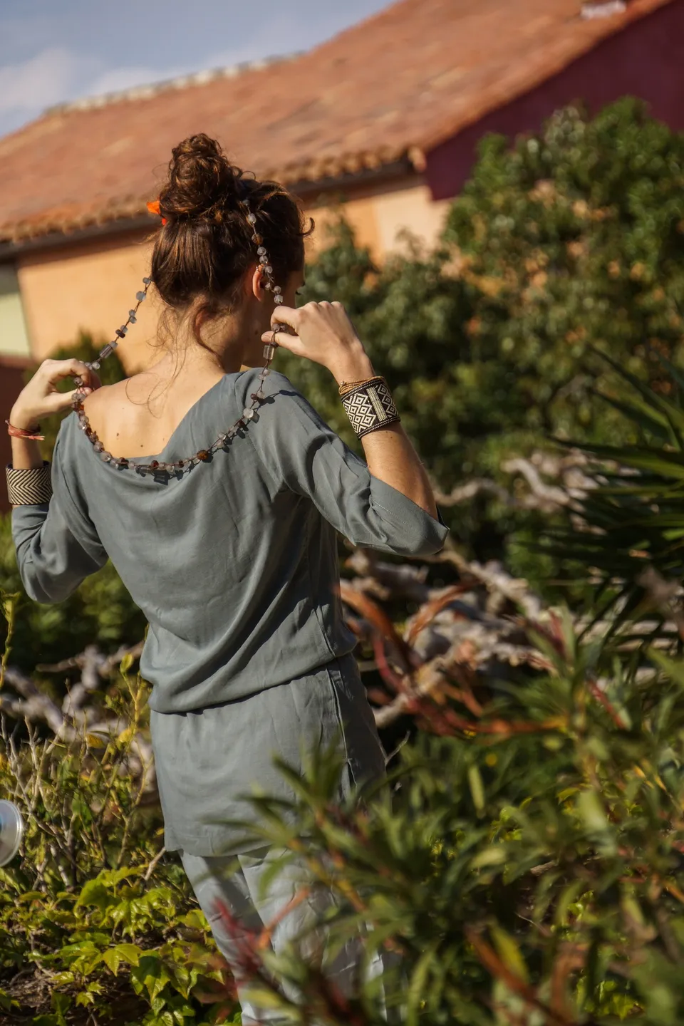 Femme en tunique grise et pantalon clair parmi les jardins de Porquerolles.