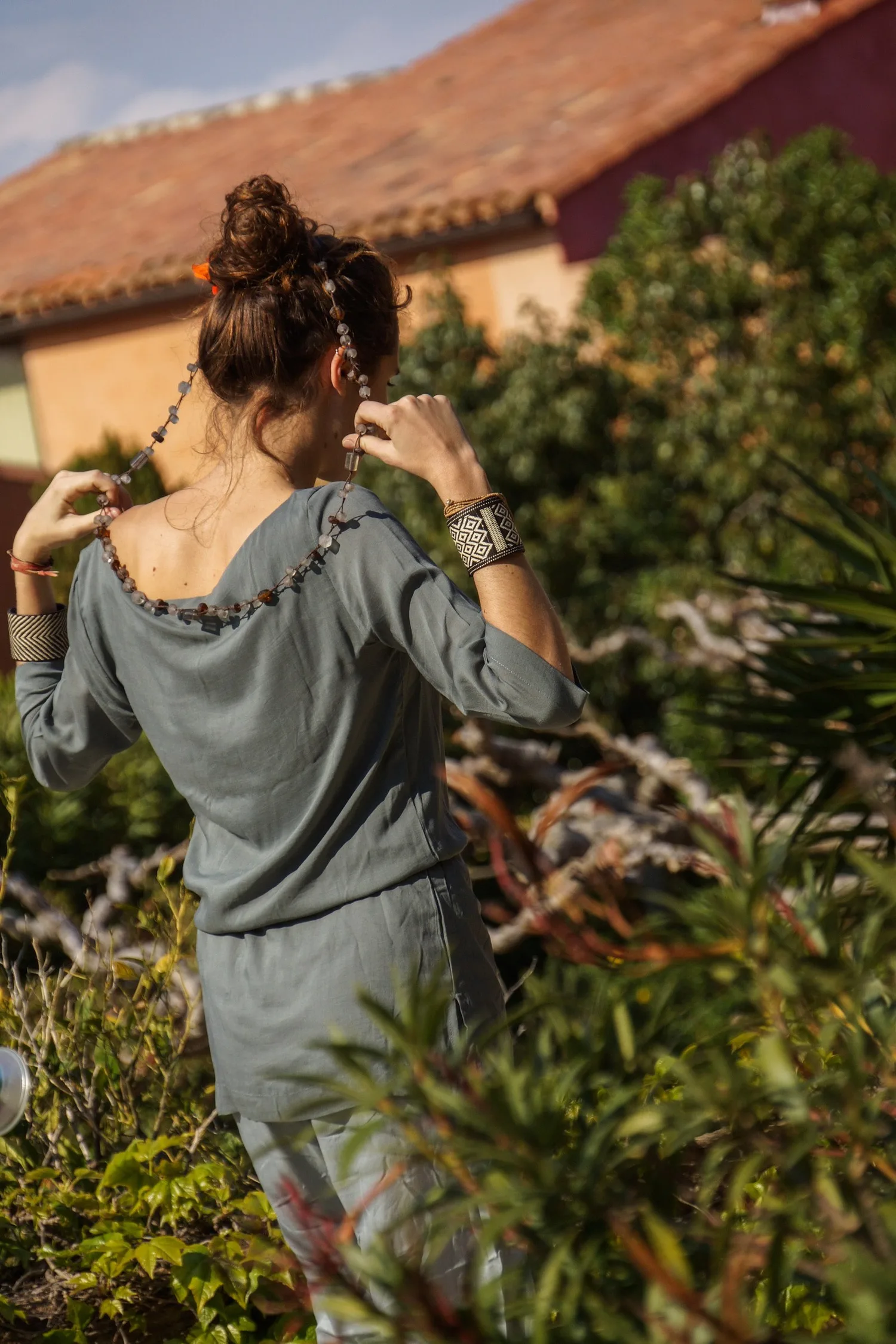 Femme en tunique grise et pantalon clair parmi les jardins de Porquerolles.