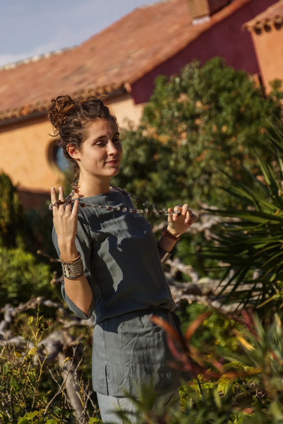 Femme en tunique grise et pantalon clair parmi les jardins de Porquerolles.