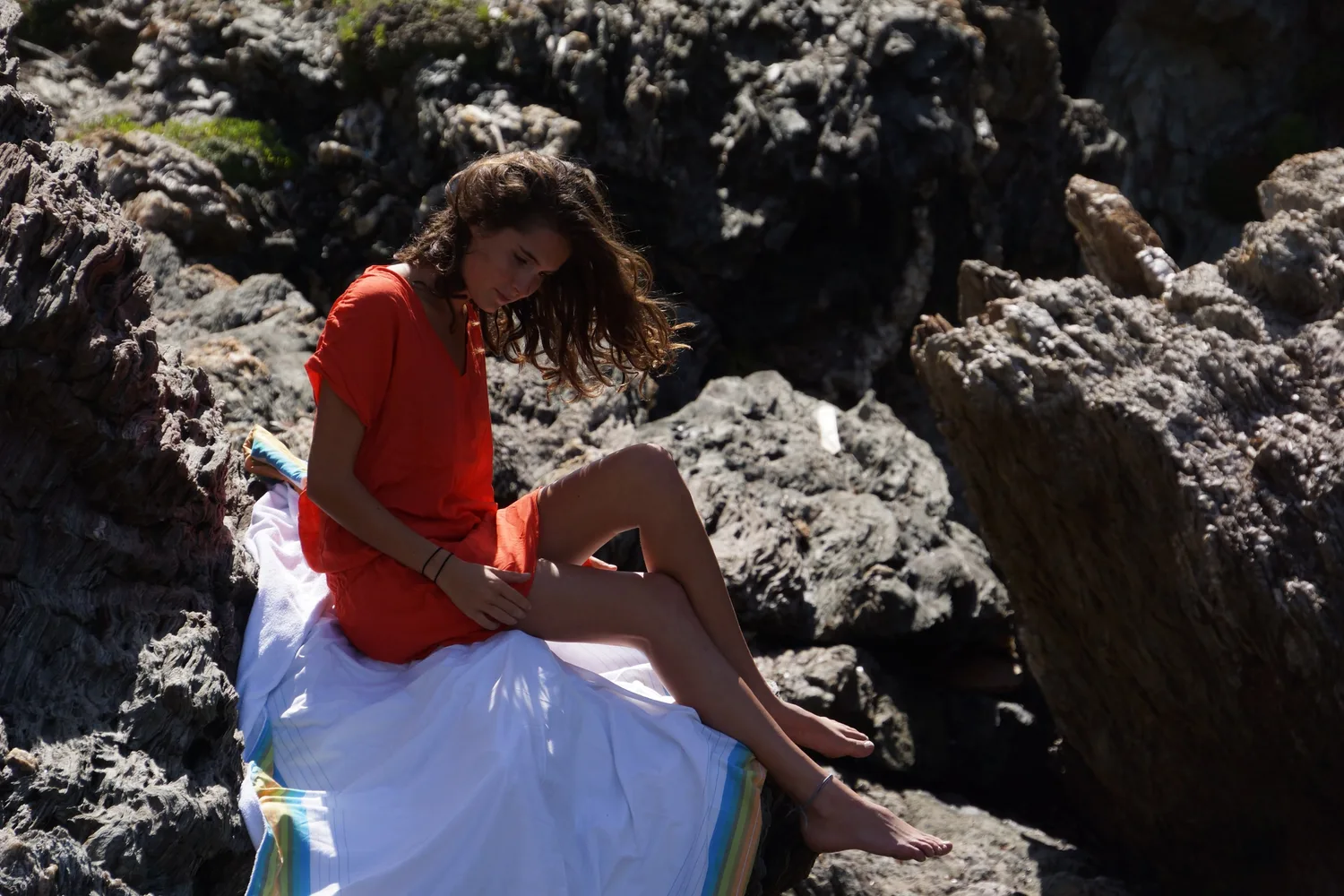 Femme en robe orange assise sur les rochers de Porquerolles.