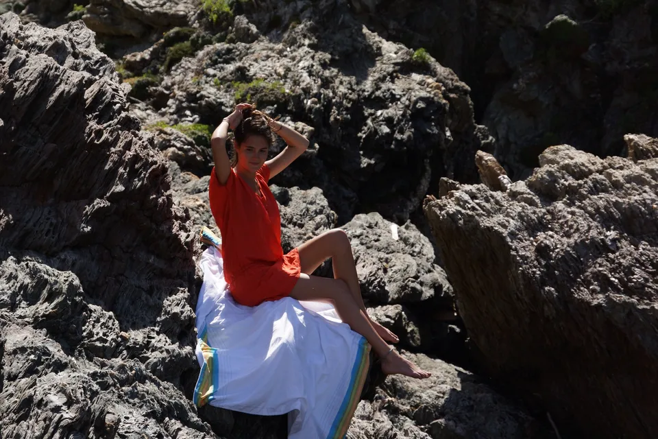 Femme en robe orange assise sur les rochers de Porquerolles.