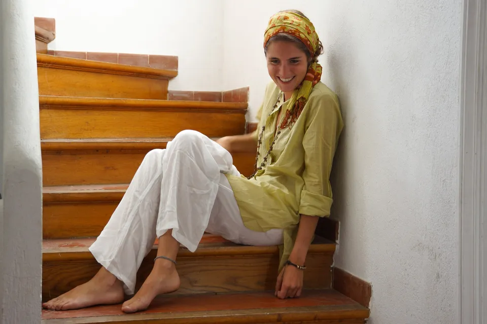 Femme en blouse claire et pantalon blanc assise dans un escalier à Porquerolles.