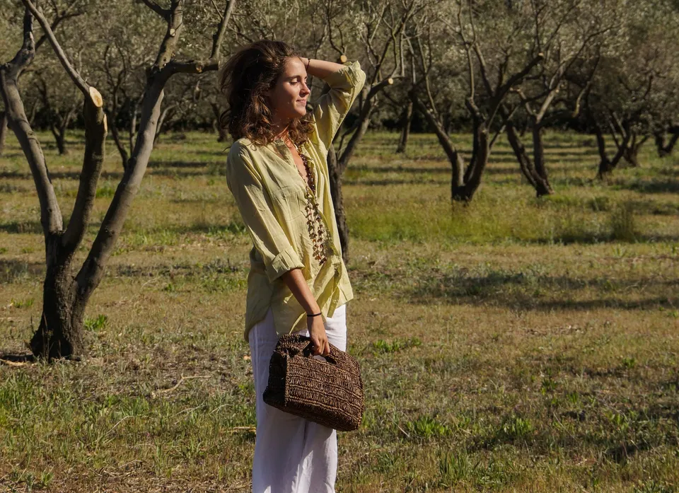 Femme en blouse claire et pantalon blanc dans une oliveraie à Porquerolles.