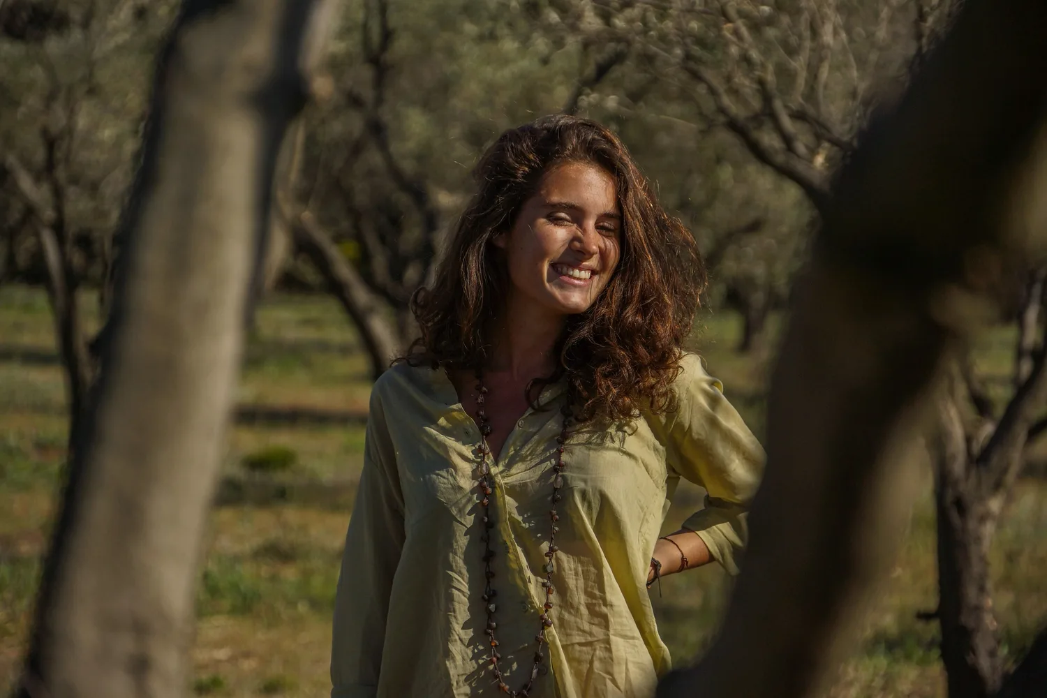 Femme en blouse claire et pantalon blanc dans une oliveraie à Porquerolles.