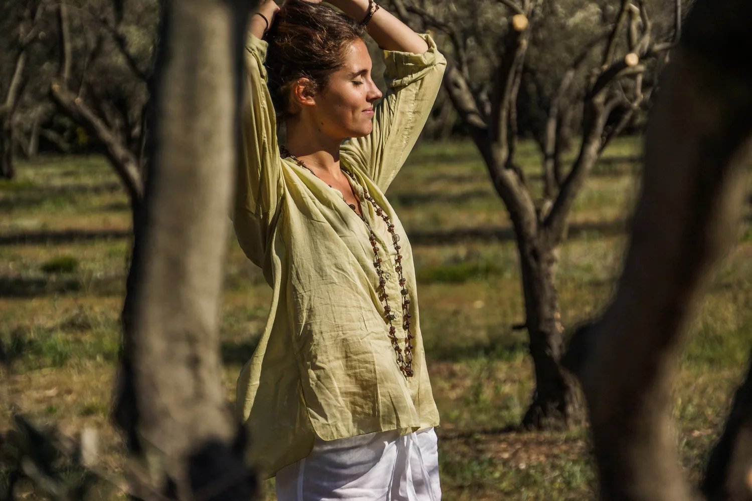 Femme en blouse claire et pantalon blanc dans une oliveraie à Porquerolles.