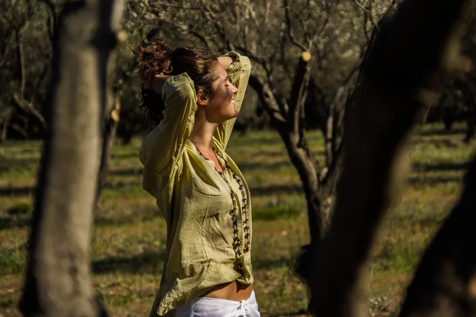 Femme en blouse claire et pantalon blanc dans une oliveraie à Porquerolles.