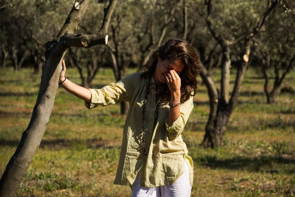 Femme en blouse claire et pantalon blanc dans une oliveraie à Porquerolles.