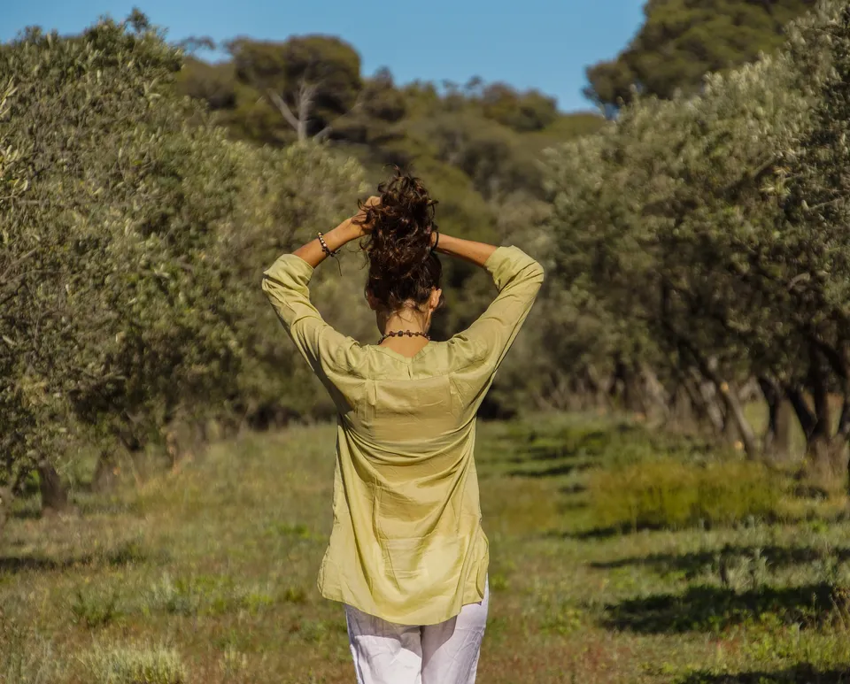 Femme en blouse claire et pantalon blanc dans une oliveraie à Porquerolles.