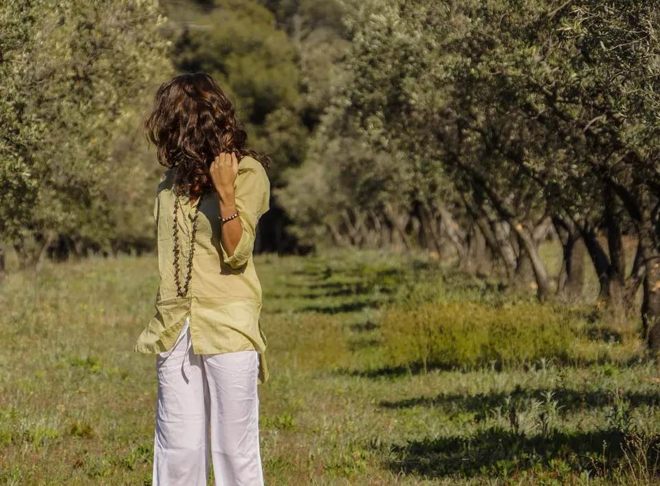 Femme en blouse claire et pantalon blanc dans une oliveraie à Porquerolles.