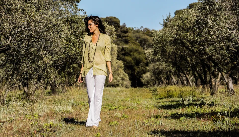 Femme en blouse claire et pantalon blanc dans une oliveraie à Porquerolles.