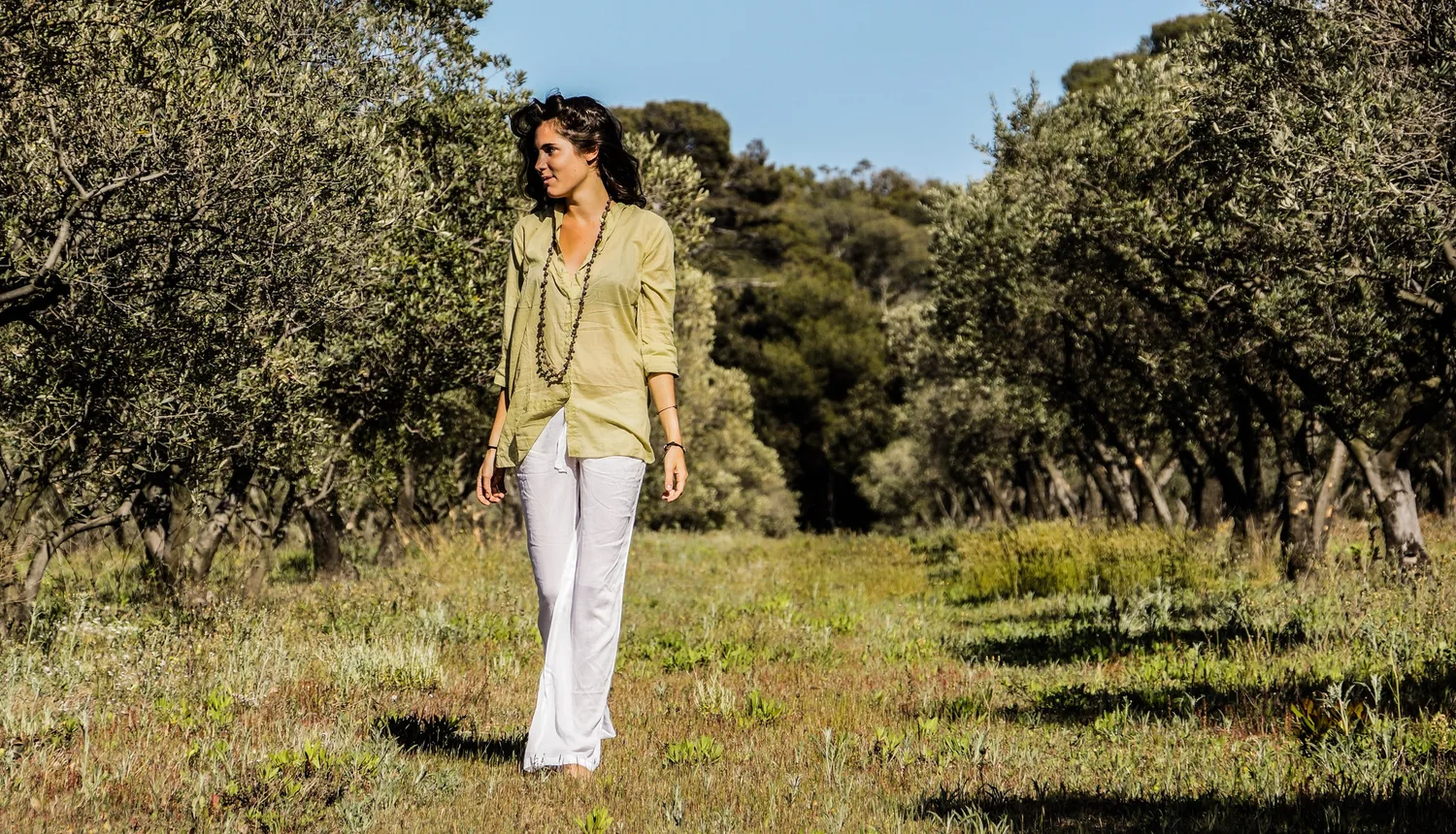 Femme en blouse claire et pantalon blanc dans une oliveraie à Porquerolles.