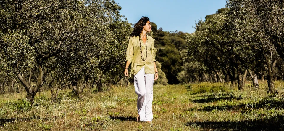 Femme en blouse claire et pantalon blanc dans une oliveraie à Porquerolles.