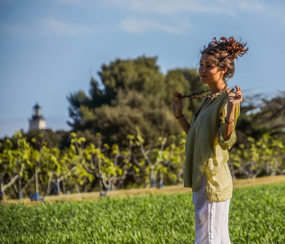 Femme en blouse claire et pantalon blanc dans une oliveraie à Porquerolles.