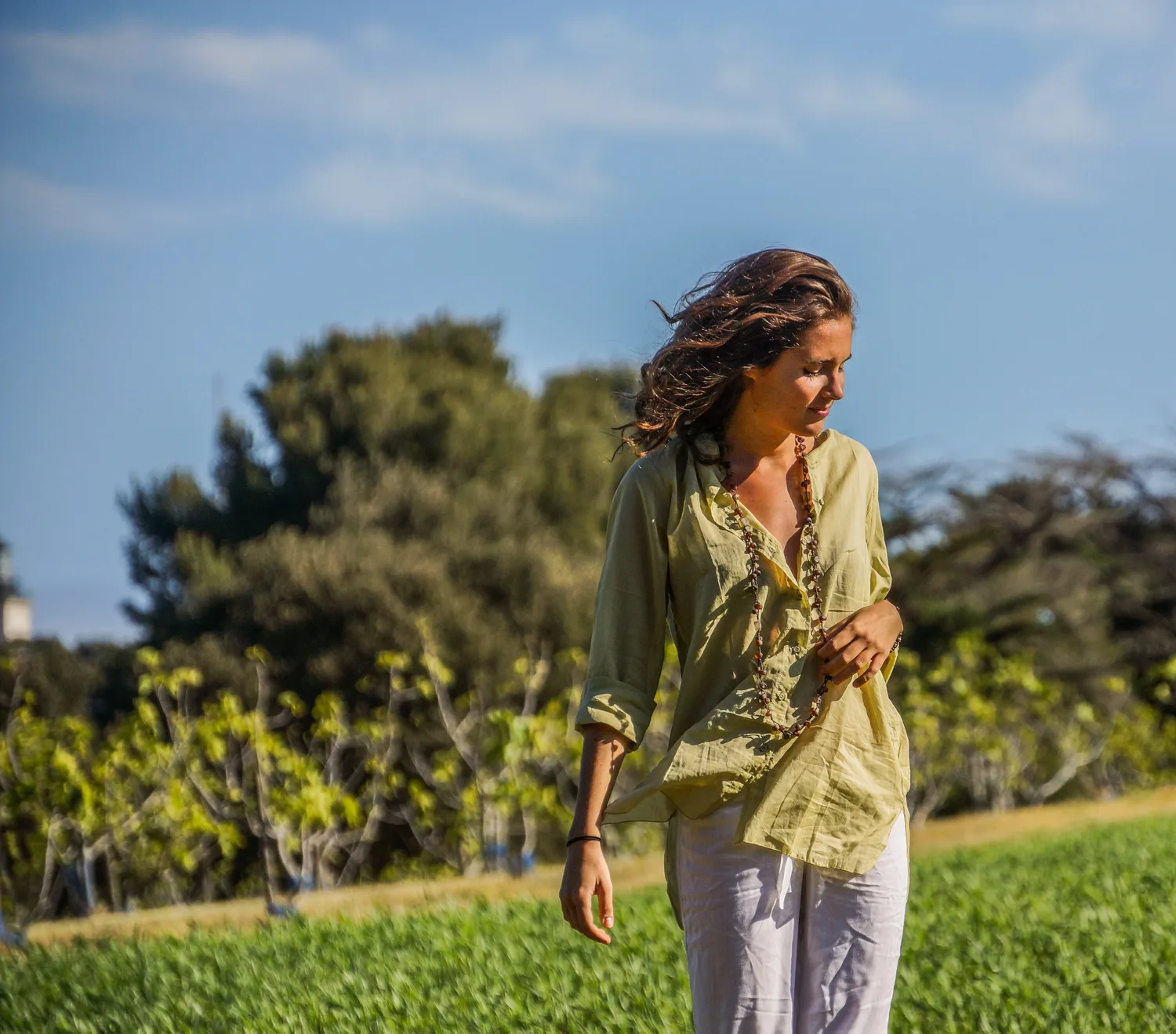 Femme en blouse claire et pantalon blanc dans une oliveraie à Porquerolles.