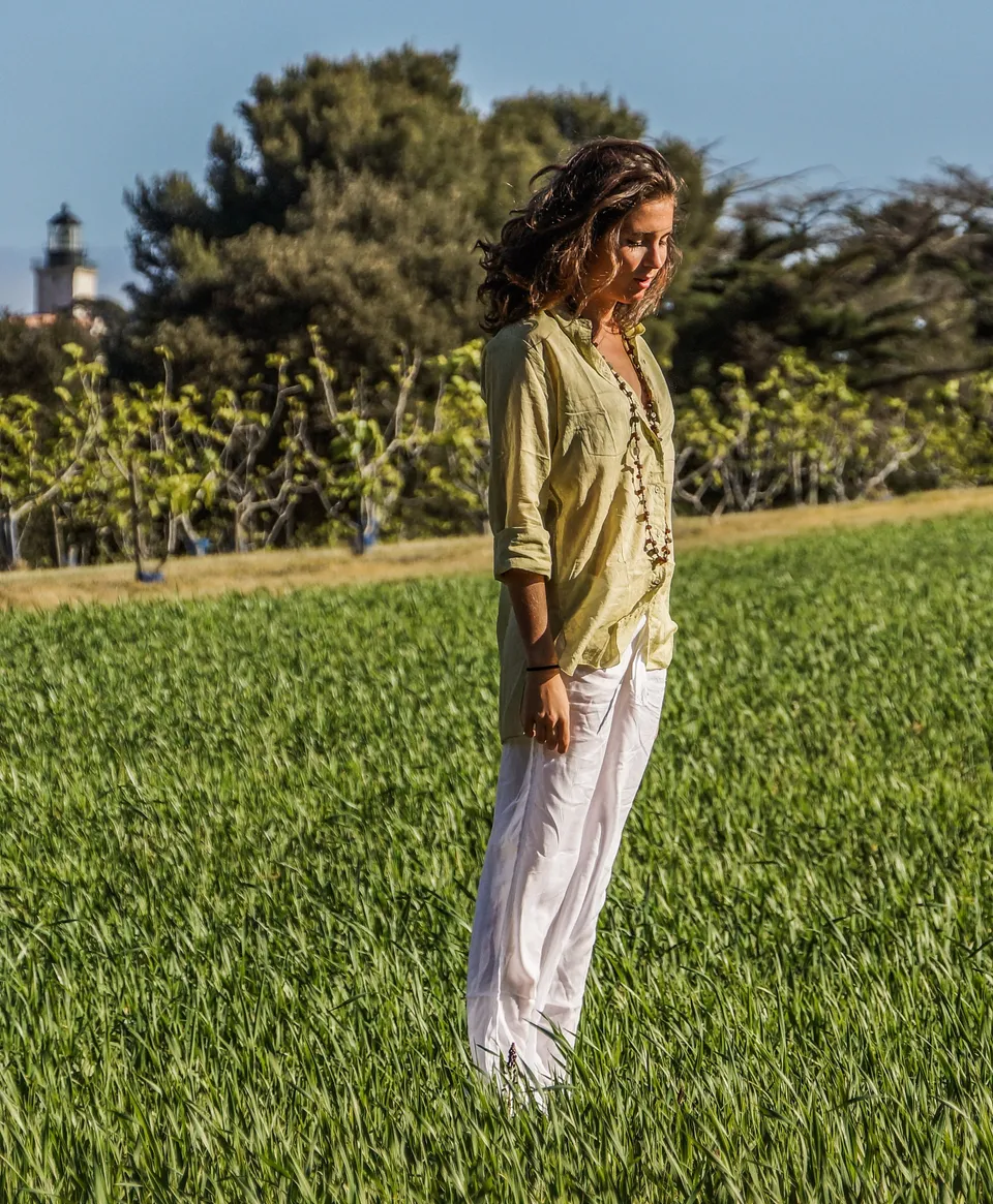 Femme en blouse claire et pantalon blanc dans une oliveraie à Porquerolles.