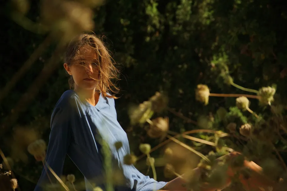 Femme en chemise de coton bleu vue à travers des herbes sèches et des chardons, lumière filtrée dans le maquis à Porquerolles.