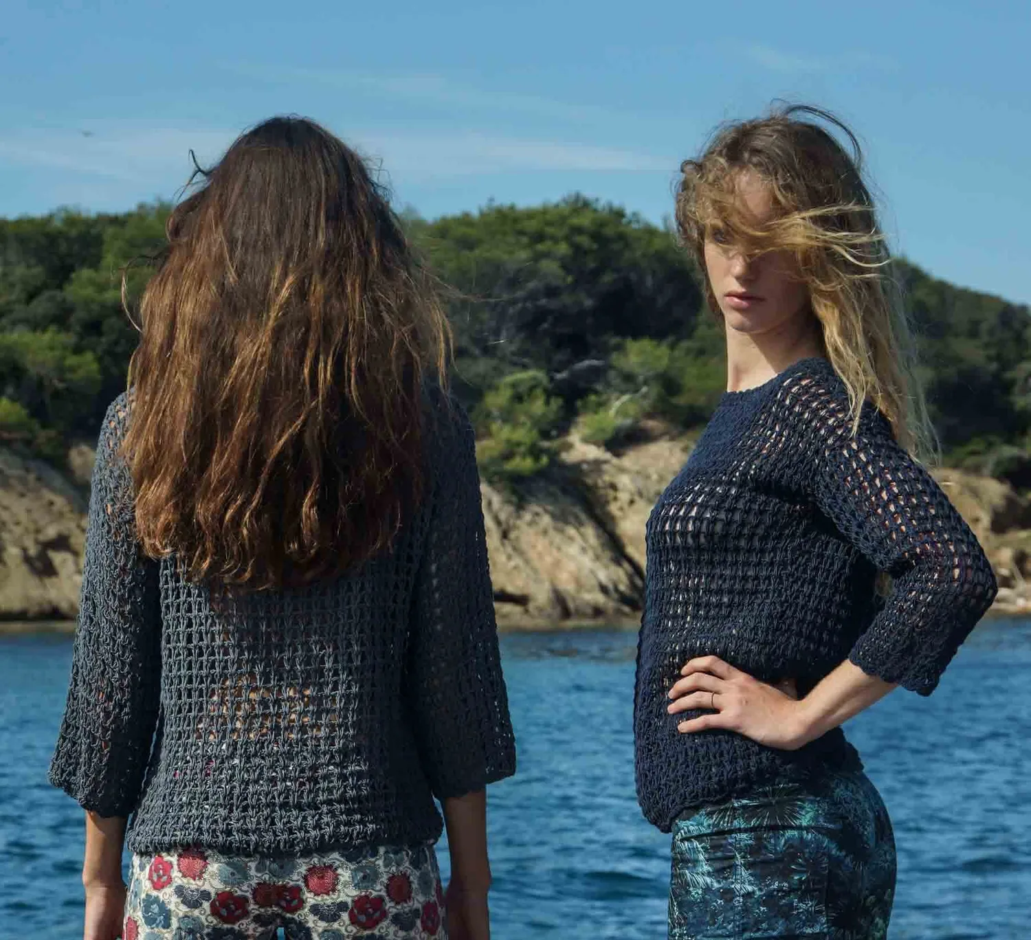 Deux femmes en pulls de crochet marine devant une crique aux eaux bleues, l'une de dos et l'autre de face, à Porquerolles.