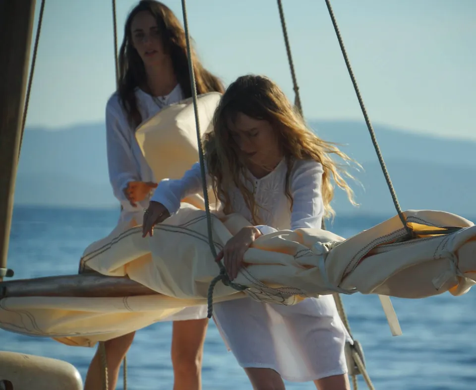 Deux femmes en coton blanc sur un voilier, l'une pliant la voile, l'autre debout, à Porquerolles.