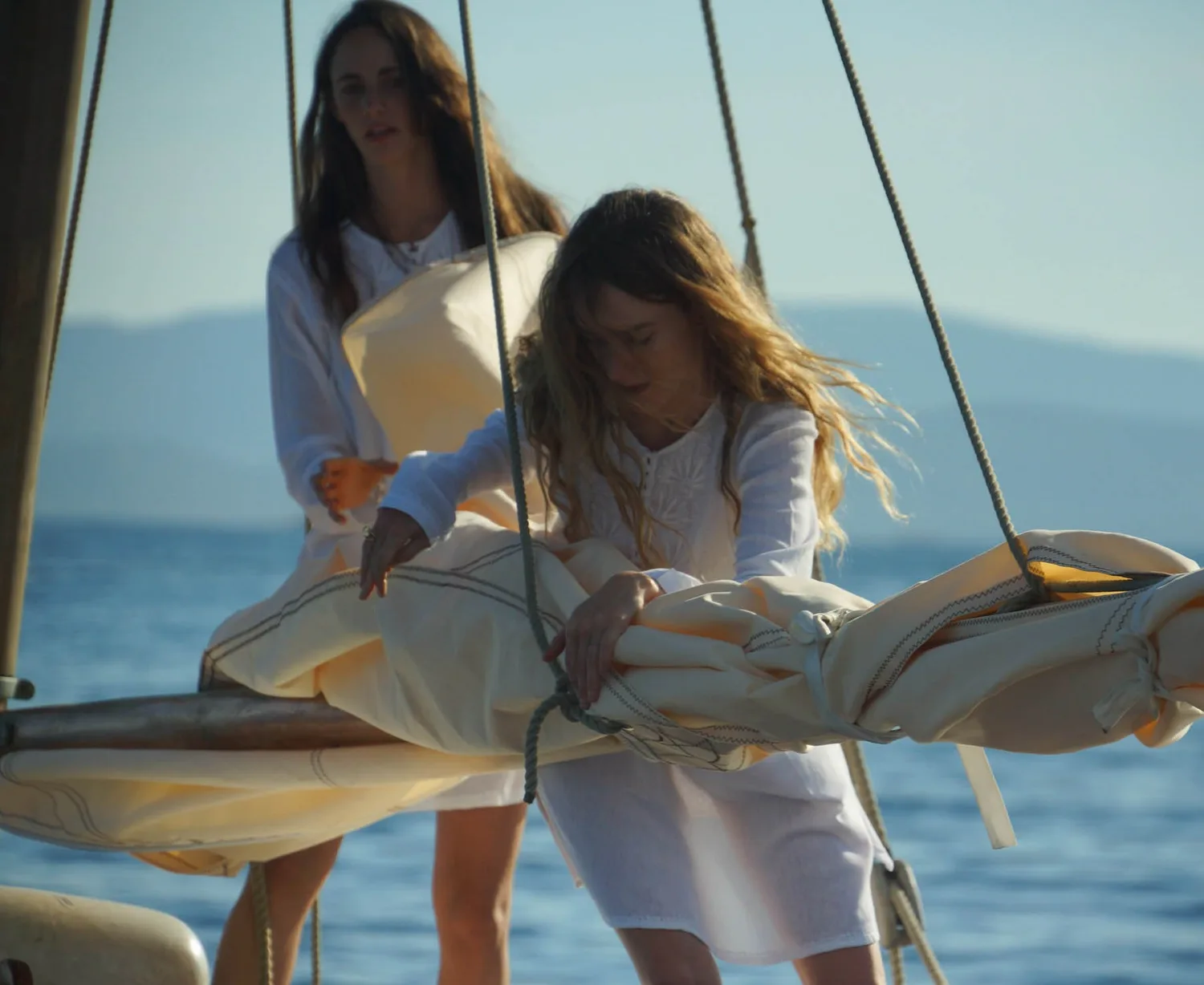 Deux femmes en coton blanc sur un voilier, l'une pliant la voile, l'autre debout, à Porquerolles.
