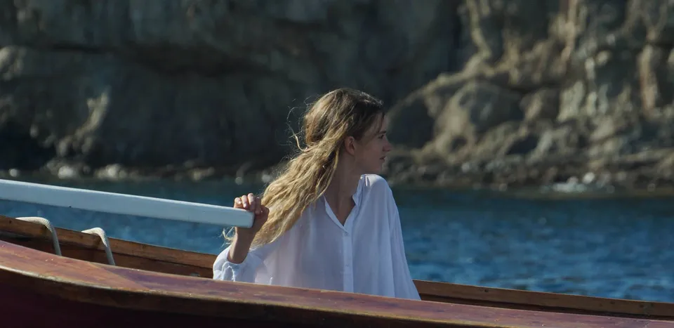 Femme de profil en chemise de coton blanc ramant, falaise de la côte en arrière-plan, à Porquerolles.