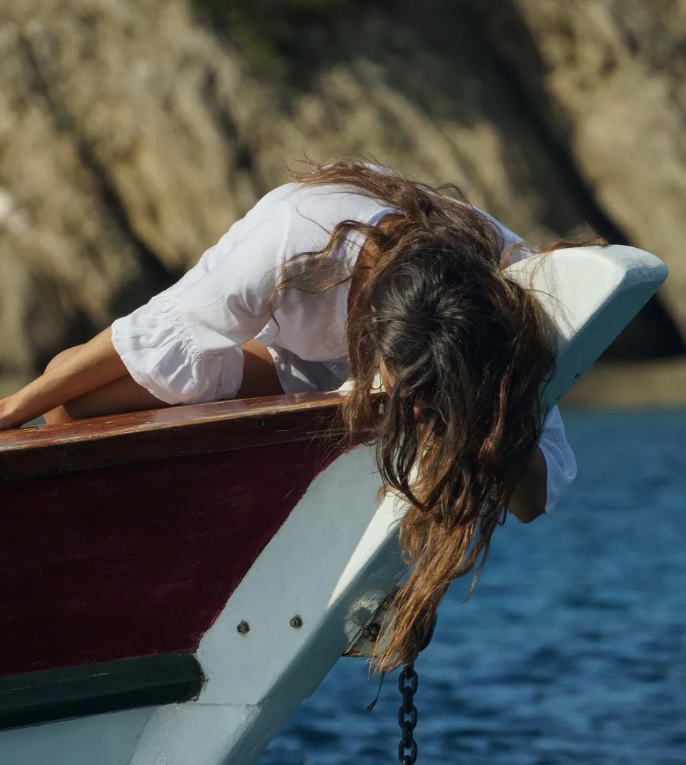 Femme en chemise de coton blanc penchée à la proue d'un bateau, cheveux tombant vers l'eau, chaîne d'ancre visible, à Porquerolles.