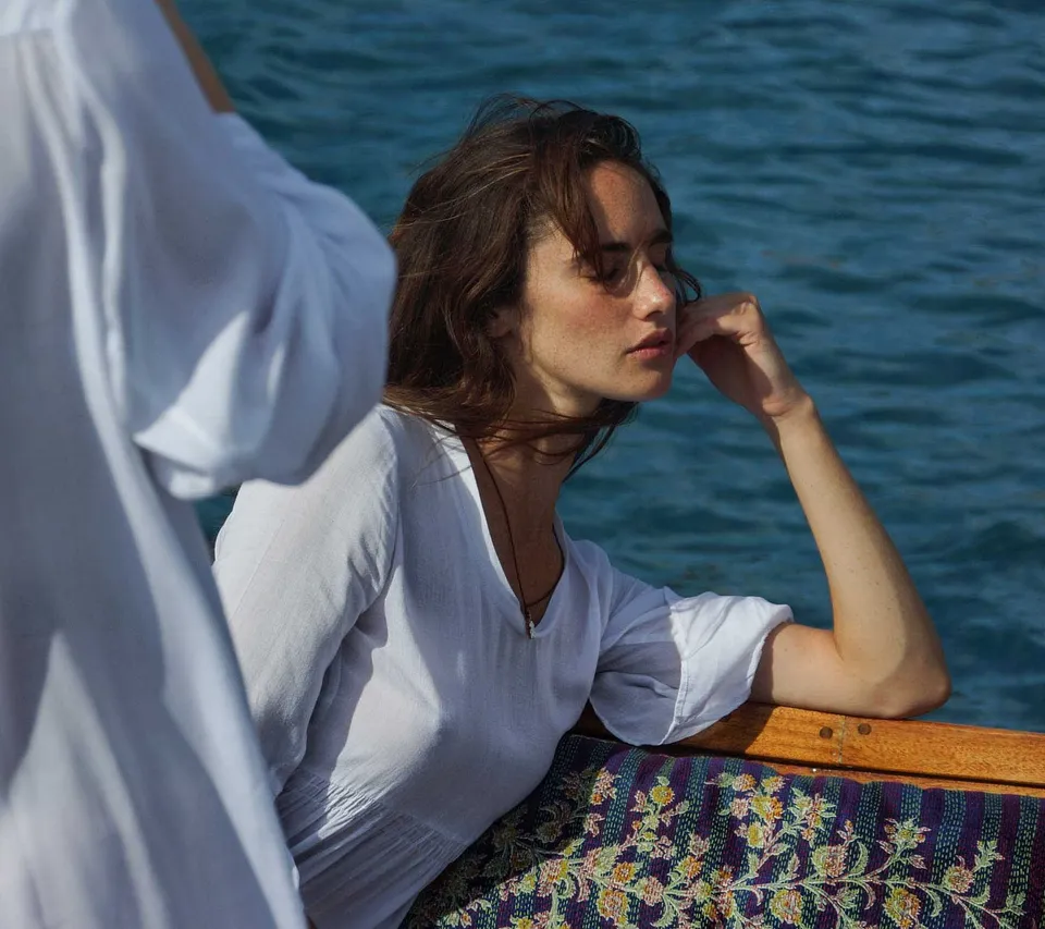Femme en chemise de coton blanc, joue posée sur la main, yeux fermés, mer en fond sur le bateau, à Porquerolles.