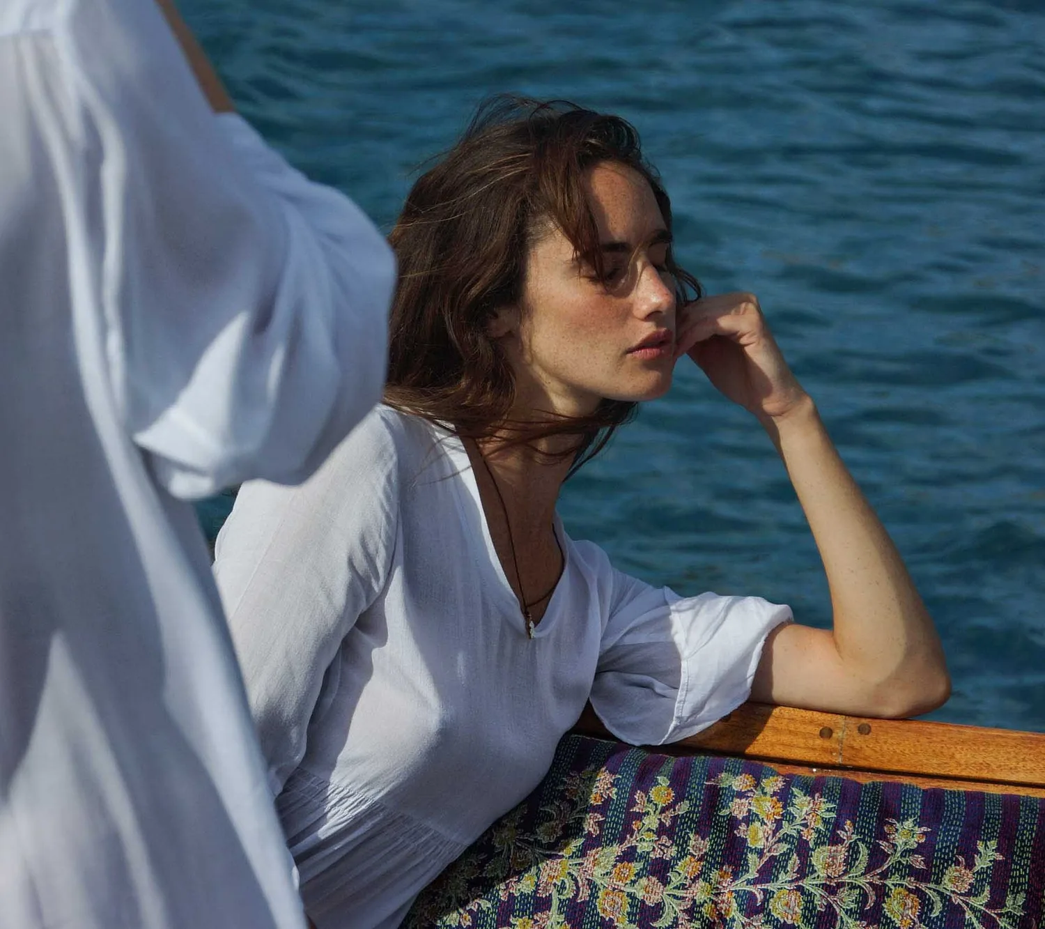 Femme en chemise de coton blanc, joue posée sur la main, yeux fermés, mer en fond sur le bateau, à Porquerolles.