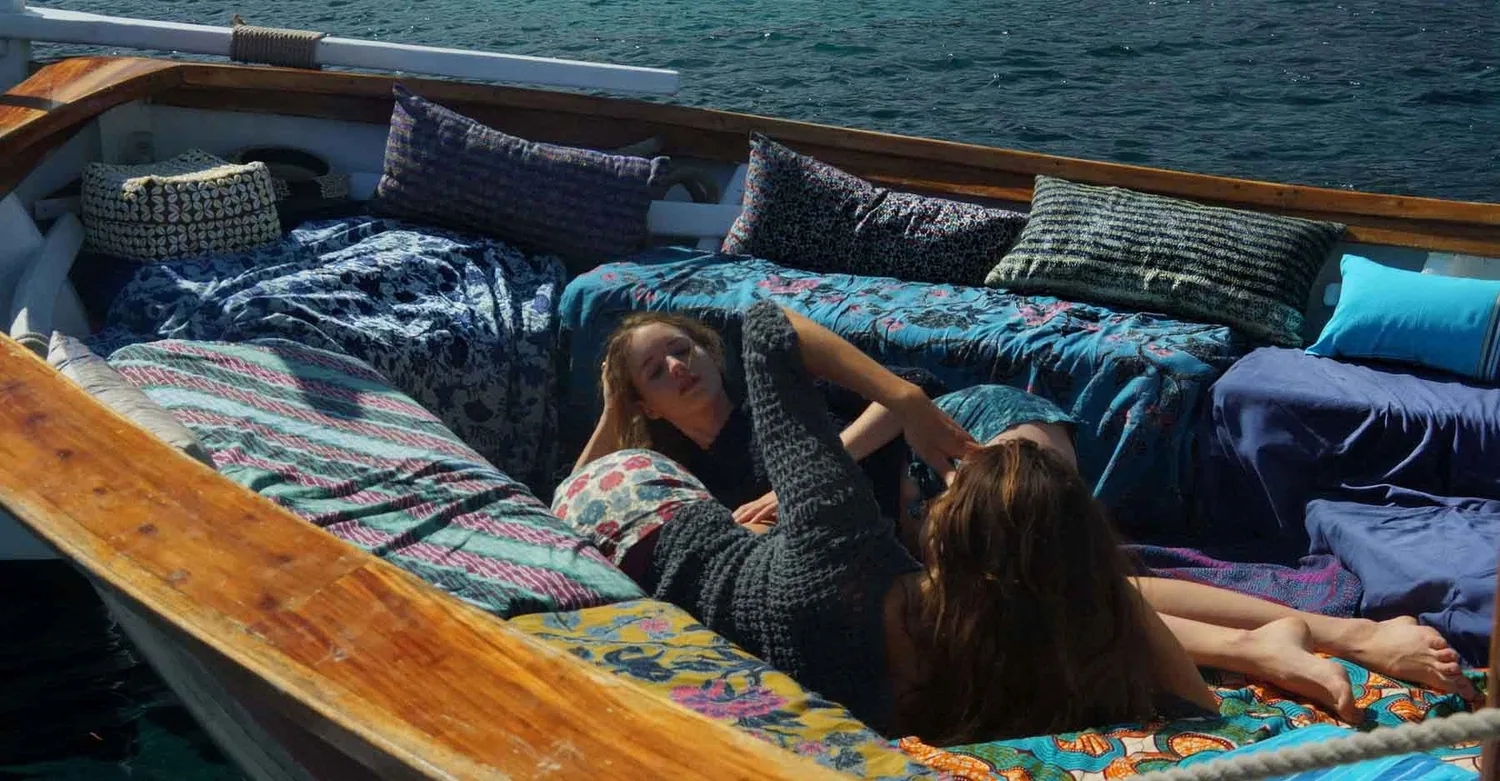 Deux femmes en pulls de crochet marine allongées sur les coussins d'un bateau, l'une la jambe levée, à Porquerolles.