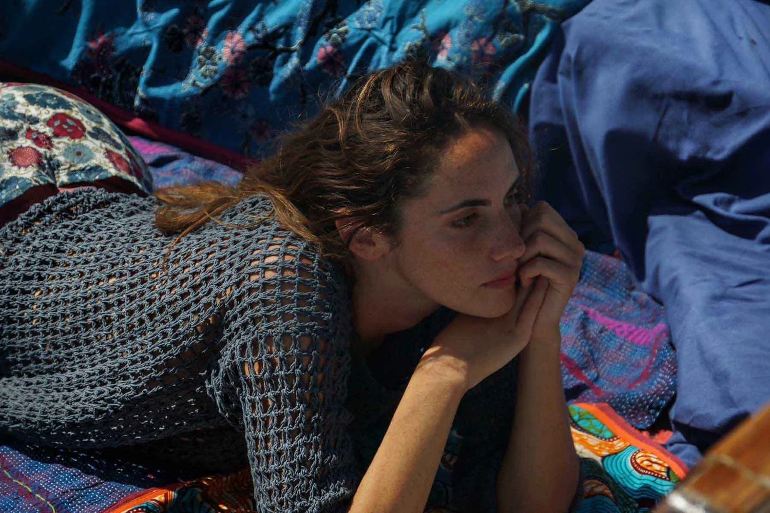 Femme en pull de crochet marine allongée sur les coussins d'un bateau, joue posée sur la main, à Porquerolles.