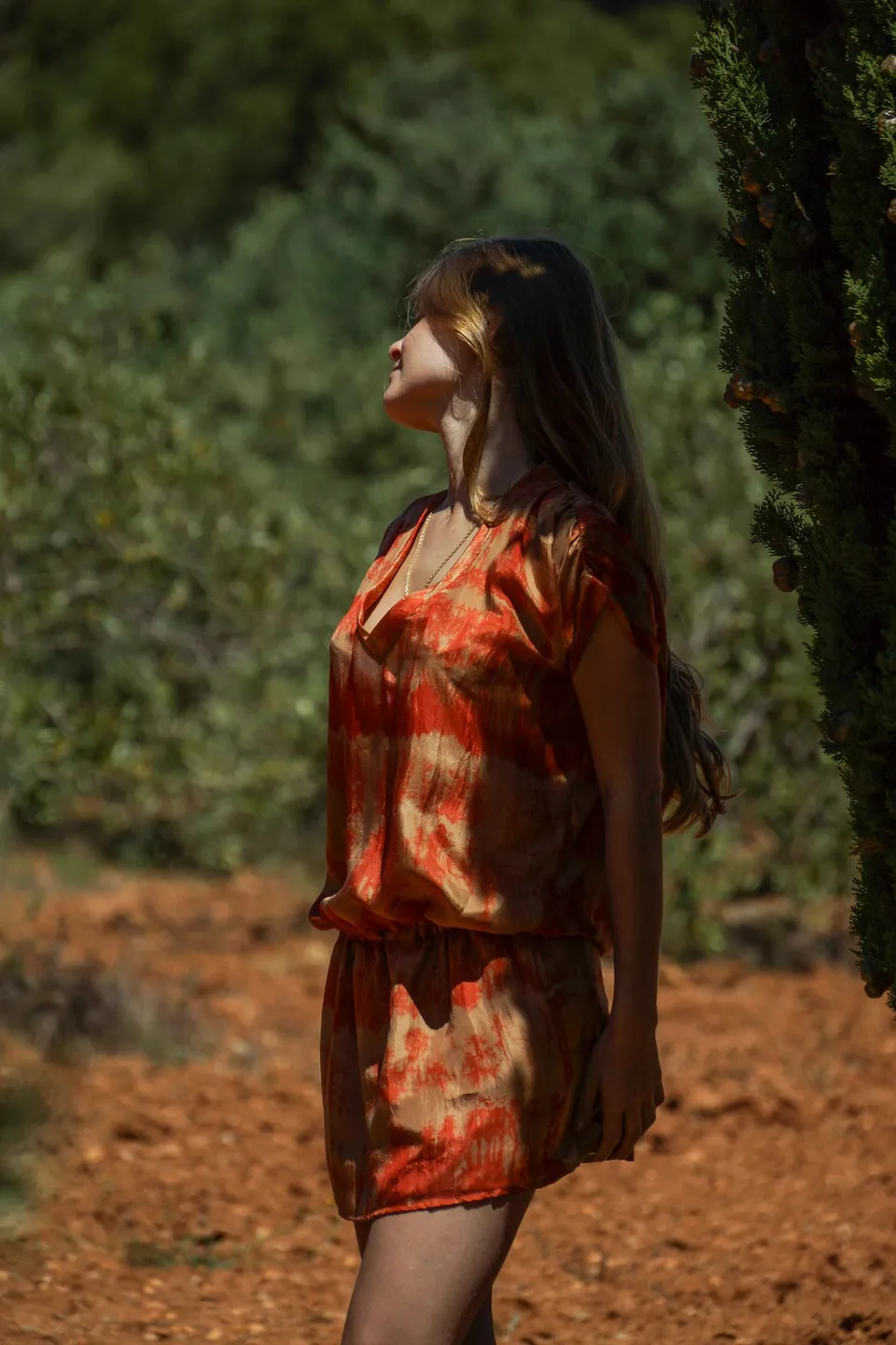 Profil d'une femme en robe tie-dye orange et beige dans le maquis dense et ensoleillé de Porquerolles.