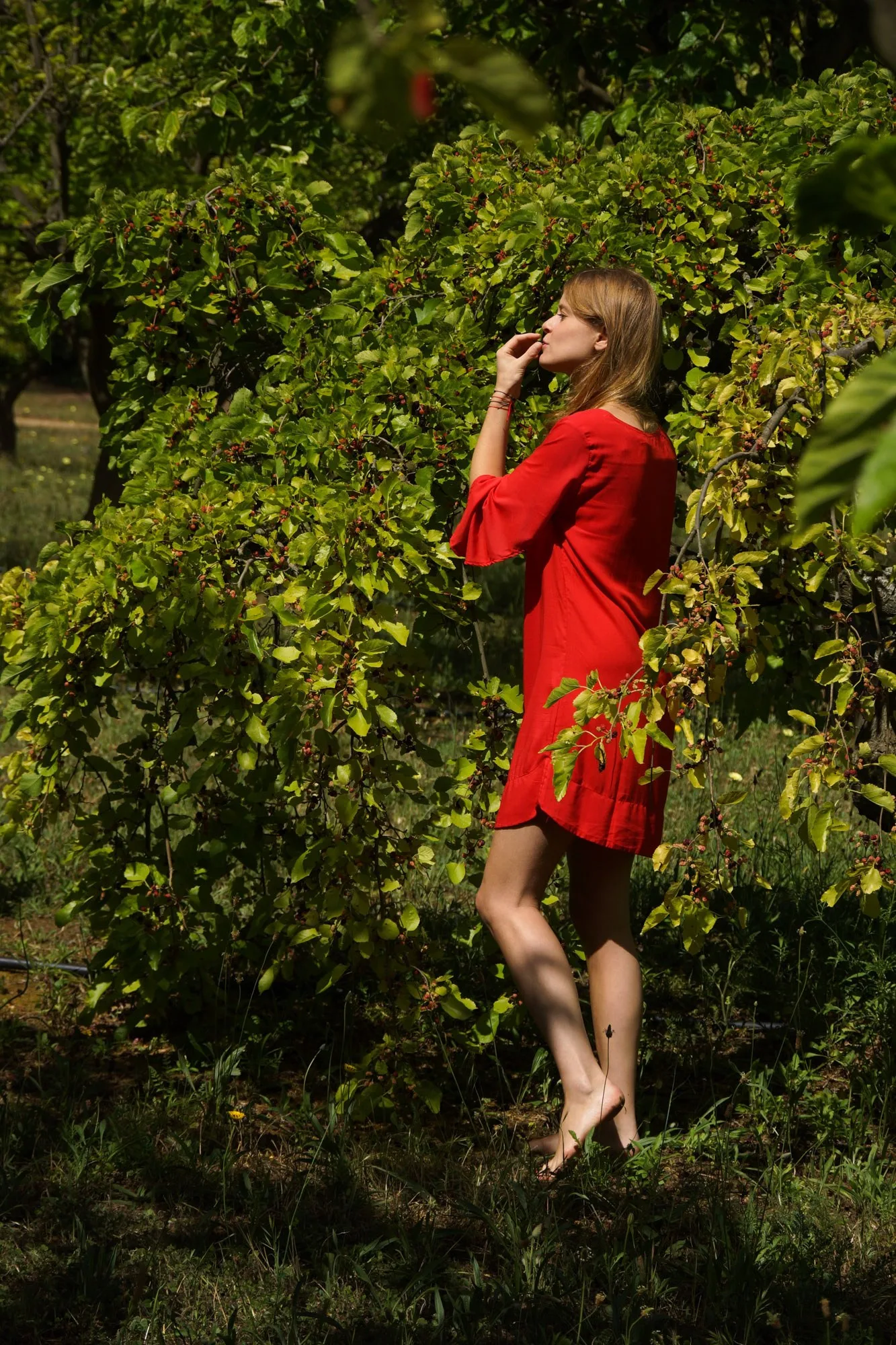 Femme en robe corail longue sur la pointe des pieds dans un jardin de Porquerolles.